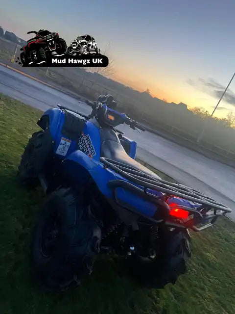 Blue all-terrain vehicle (ATV) with large, knobby tires and front and rear cargo racks.